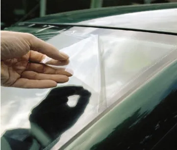 Industriel appliquant le film adhésif Tesa 4848 pour protéger temporairement un pare brise pendant la fabrication automobile